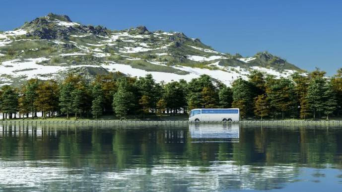Un autocar circula por una carretera, entre una montaña y un lago.