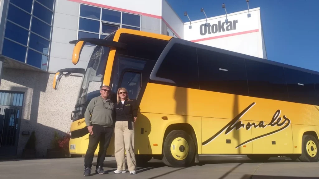 Dos personas junto a un autobús Otokar Ulyso de color amarillo