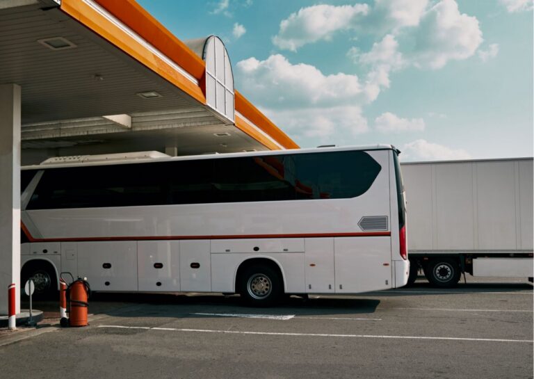 Autobús blanco repostando en una gasolinera bajo un cielo azul