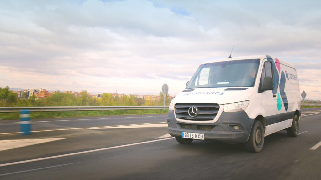 Furgoneta de Transfarm en carretera con paisaje urbano al fondo