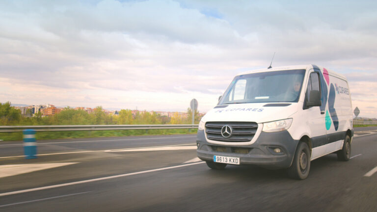 Furgoneta de Transfarm en carretera con paisaje urbano al fondo
