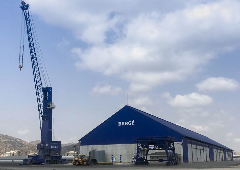 Almacén industrial de BERGÉ junto a una grúa bajo un cielo nublado.