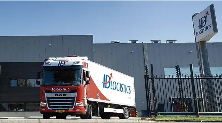 Camión de ID Logistics estacionado frente a un edificio de almacén y una señal corporativa.