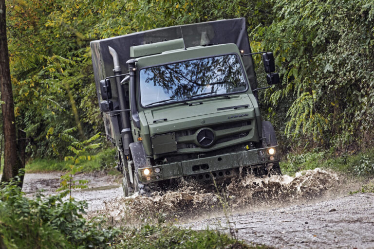 Camión Unimog verde atraviesa un camino inundado entre vegetación.