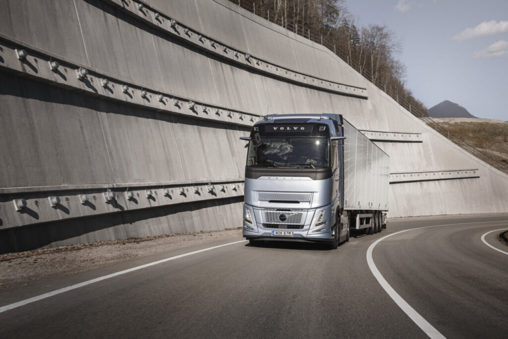 Camión Volvo FH Aero plateado con remolque circula por una carretera curva.