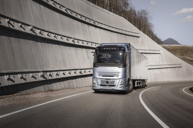 Camión Volvo FH Aero plateado con remolque circula por una carretera curva.