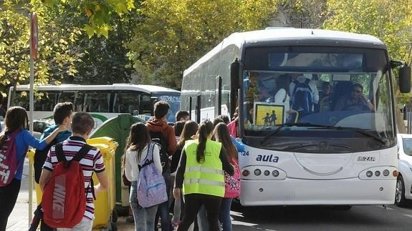Escolares con mochilas se acercan a un autobús blanco junto a otro vehículo.