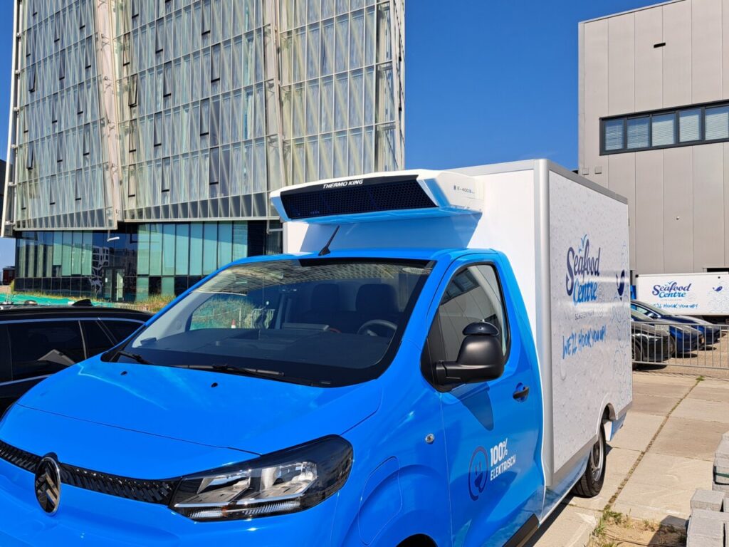 Furgoneta azul eléctrica de Seafood Centre con equipo frigorífico Thermo King frente a edificios