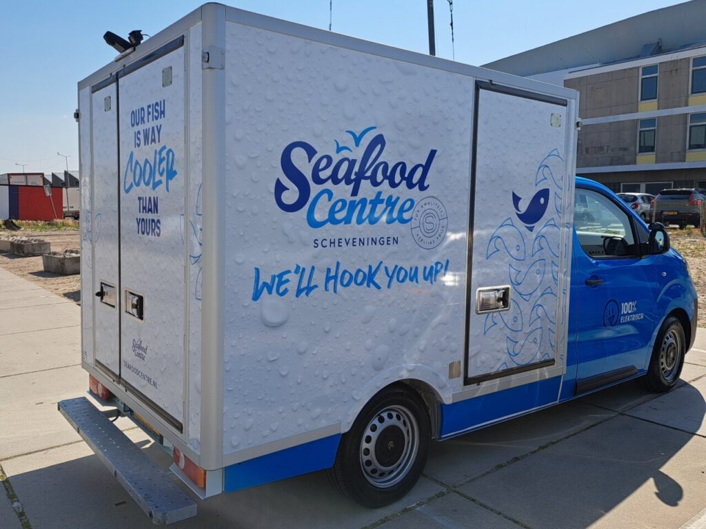 Furgoneta azul de Seafood Centre con caja blanca rotulada, estacionada junto a edificios.