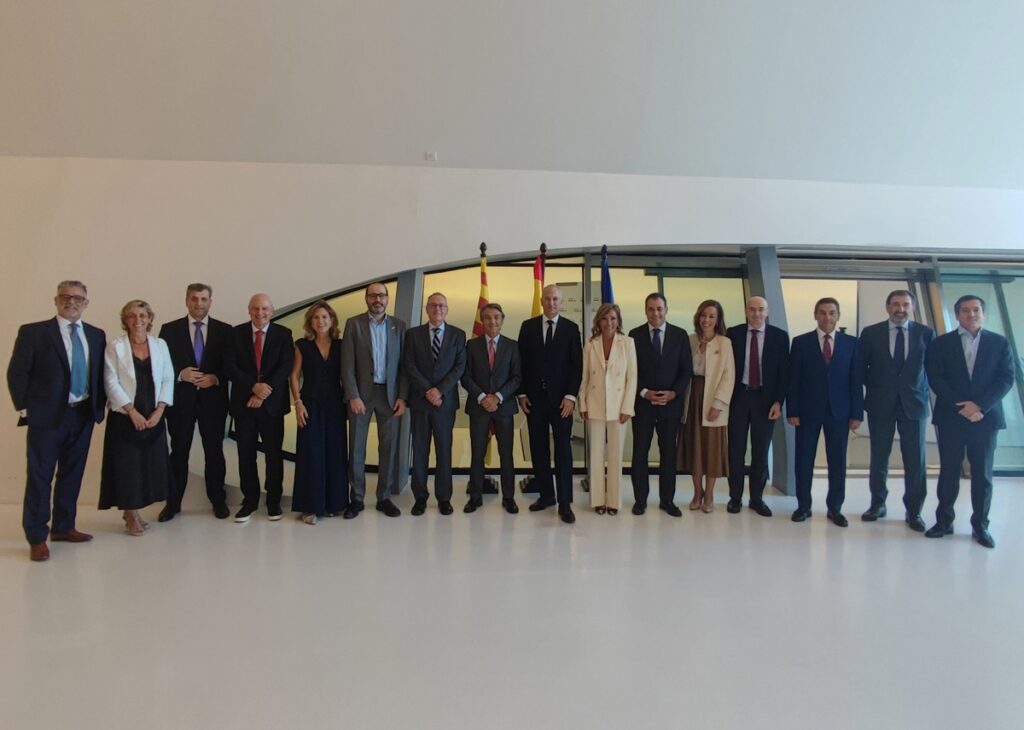 Grupo de personas posa en una sala amplia, con varias banderas detrás.
