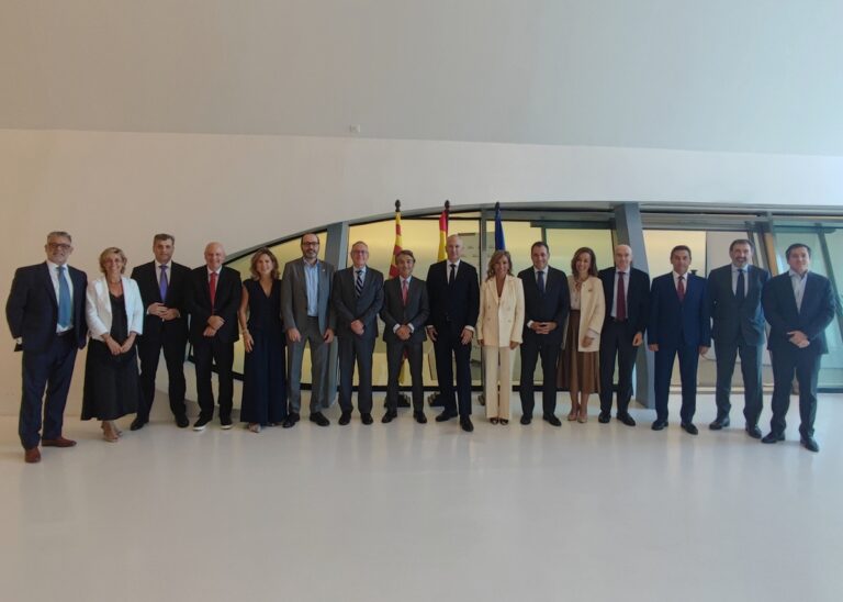 Grupo de personas posa en una sala amplia, con varias banderas detrás.
