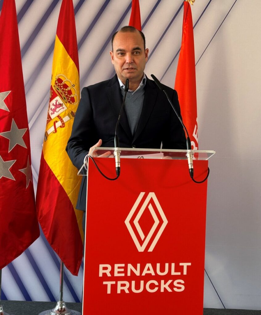 Hombre ante un atril de Renault Trucks, con banderas al fondo