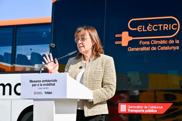 Mujer habla ante un atril junto a un autobús con rótulos sobre movilidad eléctrica.