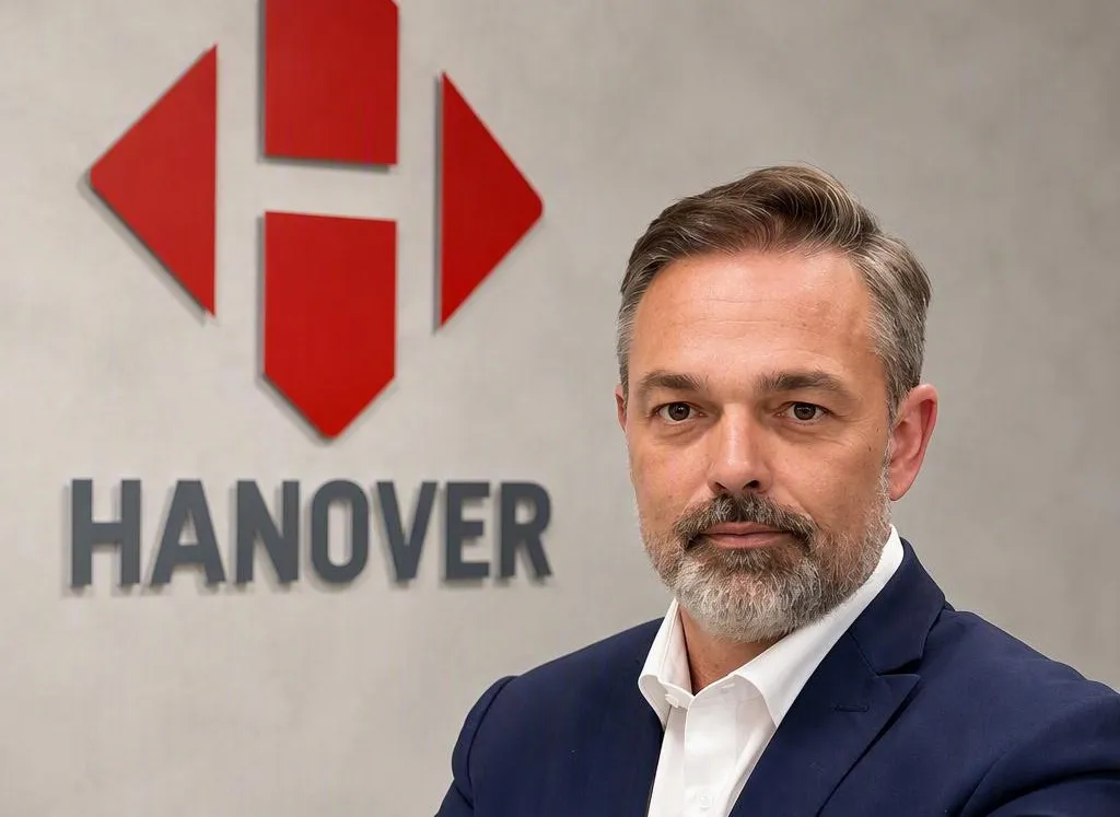Hombre con traje posa ante un logotipo de Hanover en una pared.
